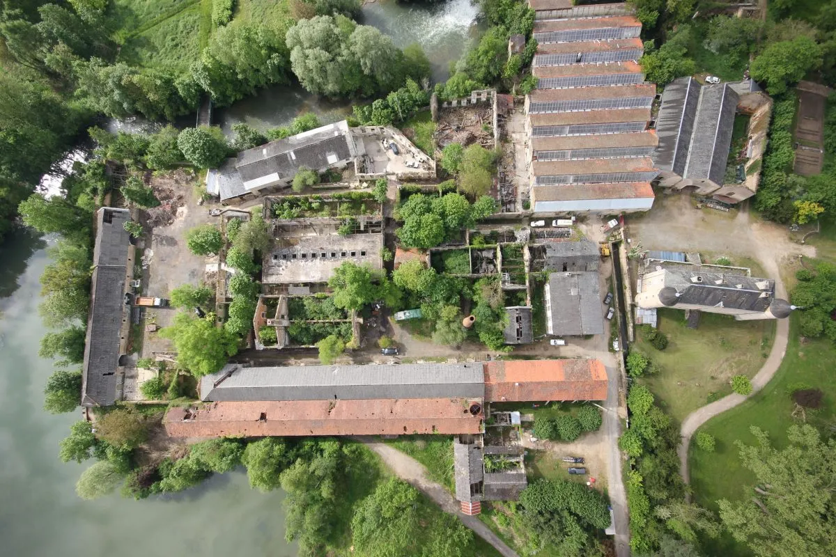 Vue aérienne du site : la rivière à gauche, les sheds du tissage en haut à droite, la cour et la cheminée au centre